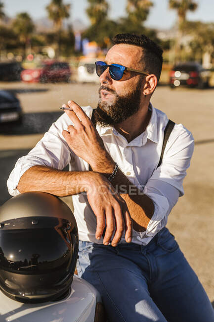 Портрет бородатого мотоцикліста з дзеркальними сонцезахисними окулярами, що спираються на його куріння шолома. — стокове фото