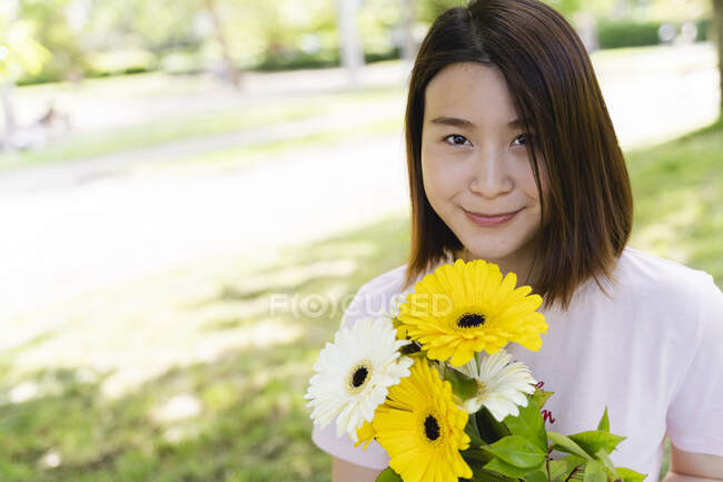 Retrato de una joven sonriente con flores en el parque - foto de stock