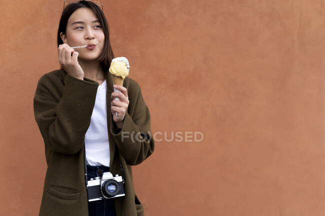 Junge Frau isst eine Eistüte an einer orangefarbenen Wand — Stockfoto