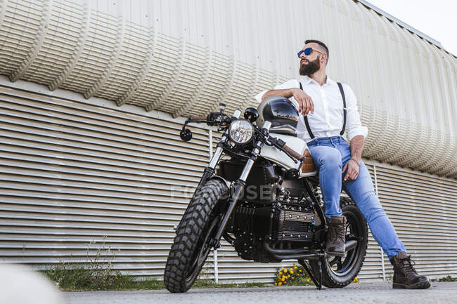 Motociclista barbudo com óculos de sol apoiados em sua moto — Fotografia de Stock