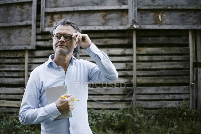 Portrait of mature man with notebook, hand on glasses - foto de stock