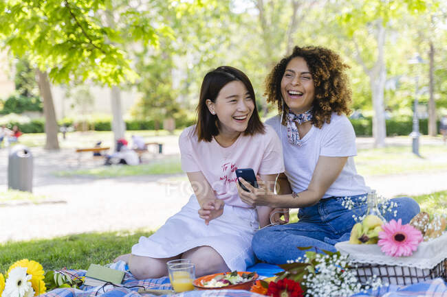 Due donne ridenti con cellulare e auricolari nel parco — Foto stock