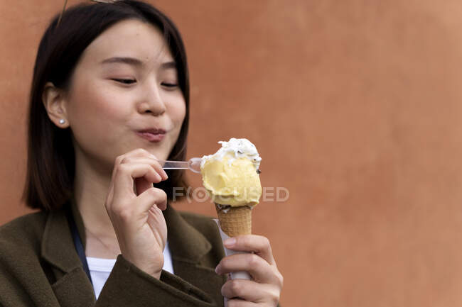 Portrait of young woman eating an ice cream cone at an orange wall — Photo de stock