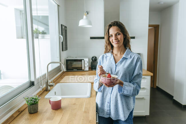 Portrait of young woman wearing pyjama eating muesli in kitchen at home — Stock Photo
