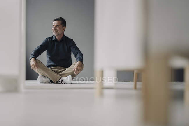 Улыбающийся взрослый бизнесмен сидит на полу — стоковое фото