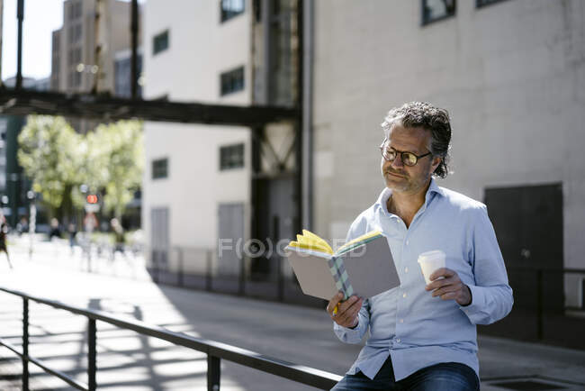 Portrait of mature man reading a book, holding coffee to go cup — Stock Photo