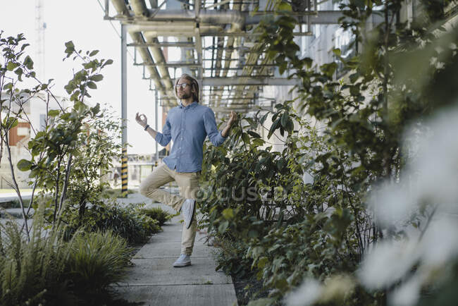 Young man meditating on pavement surrounded by plants — Stock Photo