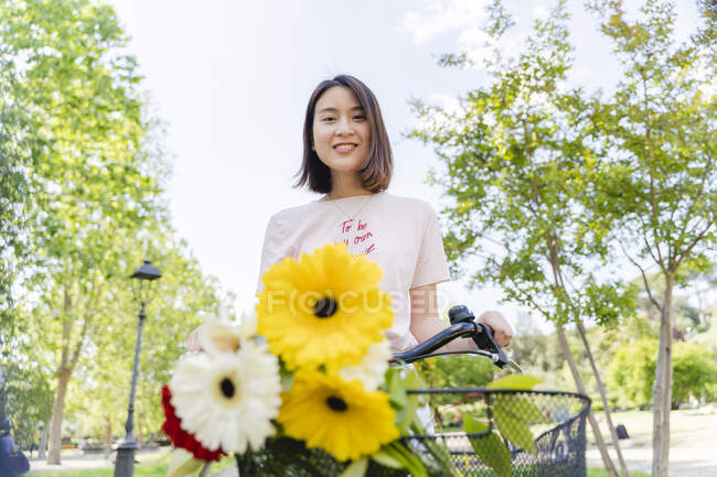 Porträt einer lächelnden jungen Frau mit Blumen und Fahrrad im Park — Stockfoto