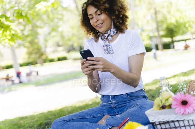 Розслабилася жінка з мобільним телефоном і навушниками, які проводили пікнік у парку. — стокове фото