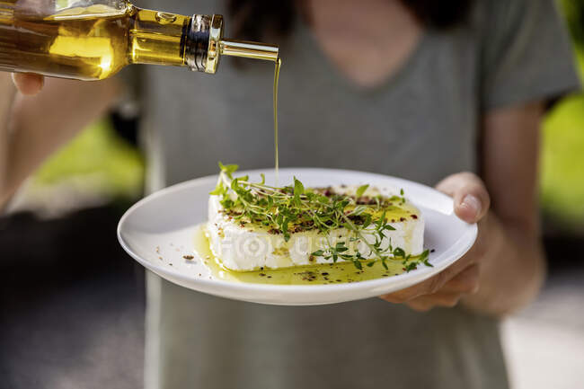Close-up of woman pouring olive oil over sheep cheese on plate — Stock Photo