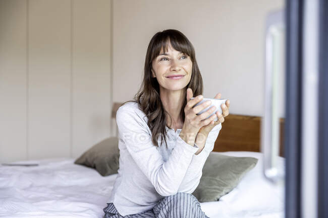 Relaxed woman with cup of coffee sitting on bed at home — Stock Photo
