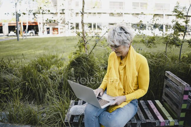 Reife Frau sitzt auf Bank im Freien mit Laptop — Stockfoto