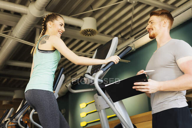 Mujer joven haciendo ejercicio en la máquina de paso en el gimnasio de fitness con entrenador personal - foto de stock