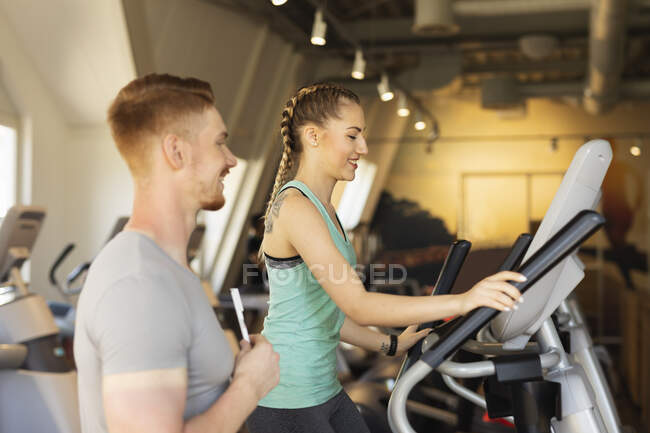 Молодая женщина, занимающаяся на степ-машине в фитнес-зале с личным тренером — стоковое фото