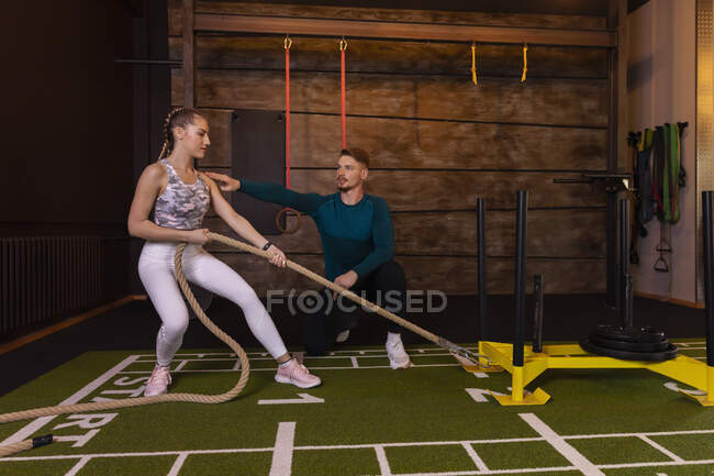 Junge Frau trainiert in Fitnessstudio mit Personal Trainer beim Seilziehen — Stockfoto