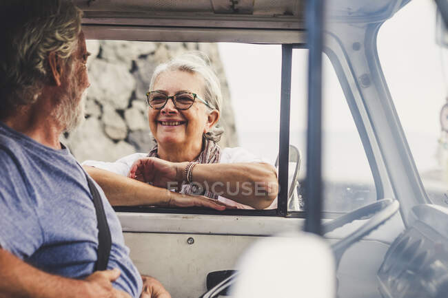 Старшая пара путешествует в винтажном фургоне, отдыхает у моря, разговаривает — стоковое фото