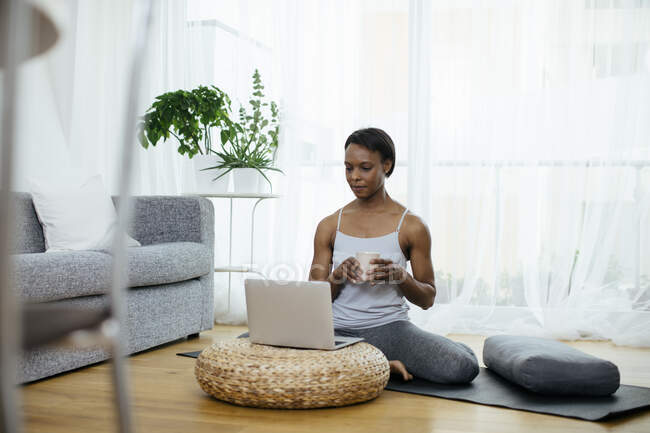 Donna seduta sul tappetino da palestra a casa con il computer portatile — Foto stock
