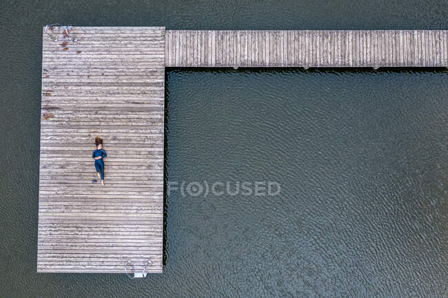 Veduta aerea di una giovane triatleta donna sdraiata sul molo di un lago — Foto stock