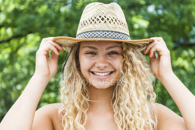 Retrato de una mujer rubia sonriente con sombrero de paja, manos sobre sombrero - foto de stock