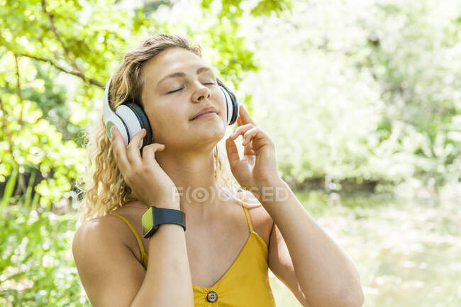Smiling woman with closed eyes listening to music at lakeside — Stock Photo