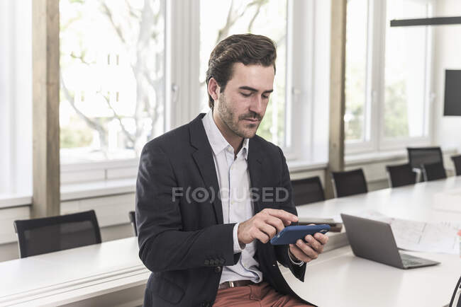 Giovane uomo d'affari seduto in sala riunioni, smartphone usig — Foto stock