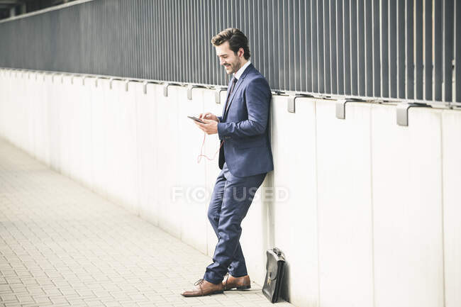 Geschäftsmann lehnt in der Stadt an einer Mauer und checkt sein Handy — Stockfoto