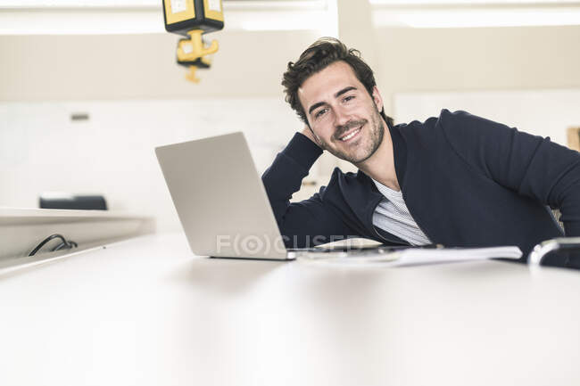Relaxed young businessman with laptop, sitting in office — Stock Photo