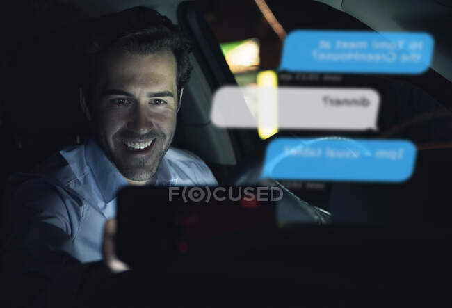 Homme d'affaires souriant utilisant un téléphone portable pour la messagerie i dans la voiture la nuit — Photo de stock