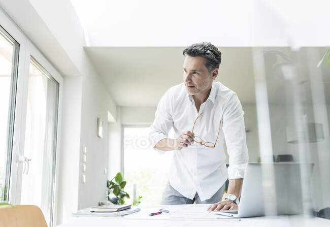 Architect working on blueprint in a bright office, using laptop — Stock Photo
