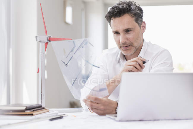 Businessma n seduto in ufficio, utilizzando il computer portatile, guardando il modello di un volano — Foto stock