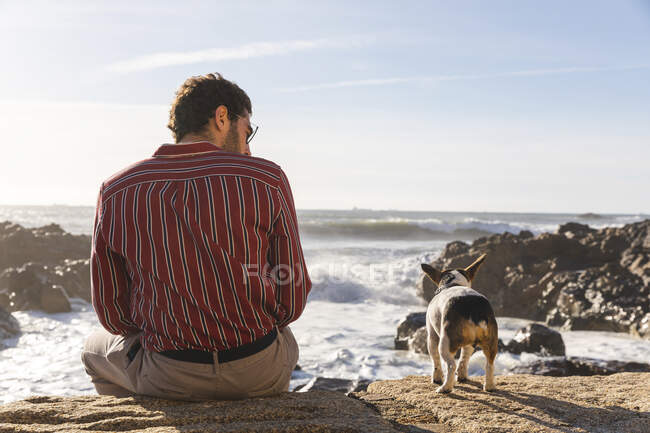 Portugal, Porto, back viwe of young man and his dog in front of the sea — Stock Photo