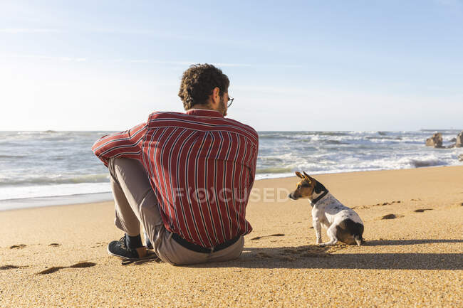 Portogallo, Porto, veduta posteriore del giovane seduto sulla spiaggia con il suo cane — Foto stock