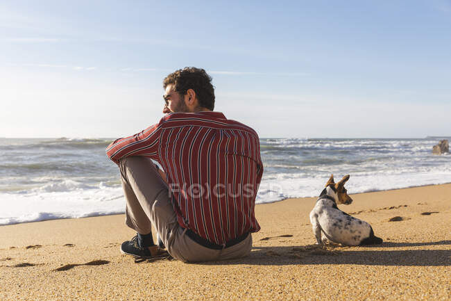 Portugal, Porto, vue arrière du jeune homme assis sur la plage avec son chien — Photo de stock