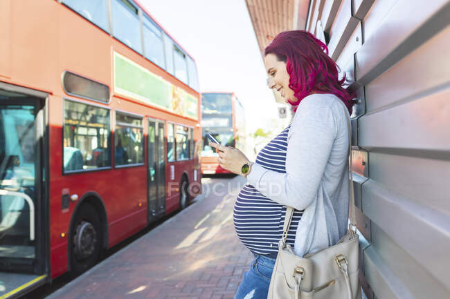Donna incinta che usa il telefono alla fermata dell'autobus — Foto stock
