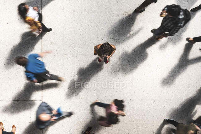 Женщина смотрит на мобильный телефон между спешащими людьми, вид сверху — стоковое фото