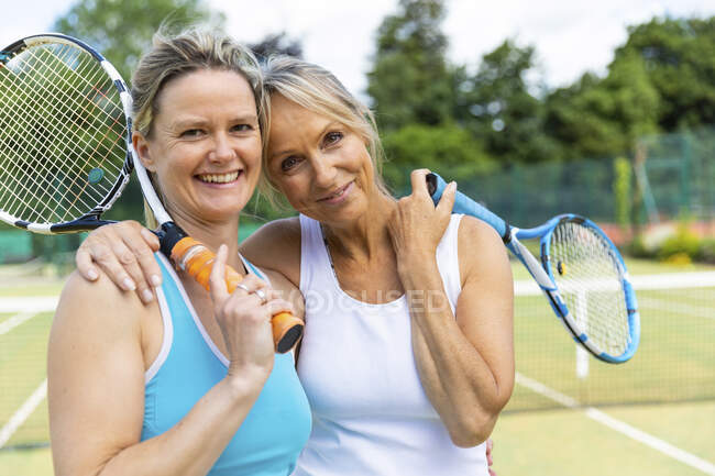 Retrato de dos mujeres maduras felices en la cancha de hierba en el club de tenis - foto de stock