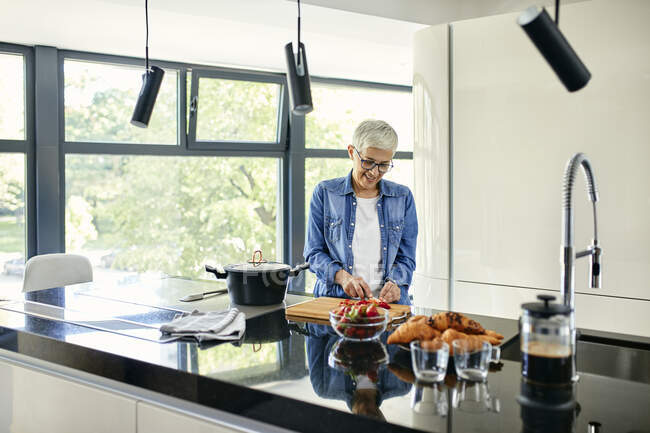 Seniorin steht in Küche und schneidet Erdbeeren — Stockfoto