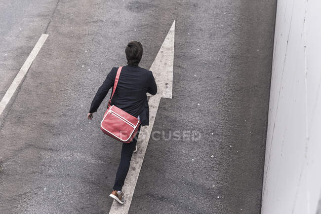 Rear view of businessman running on road with arrow sign — Stock Photo
