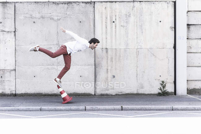 Junger Mann balanciert auf Verkehrskegel vor Betonwand — Stockfoto