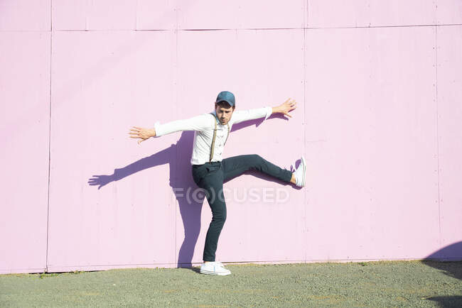 Молодой человек перед розовым строительным барьером, балансирующий на одной ноге — стоковое фото
