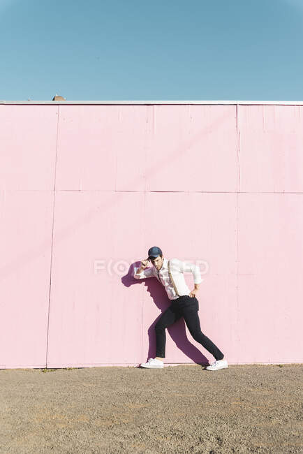 Young man in front of pink construction barrier, hand on hat, thinking — Stock Photo