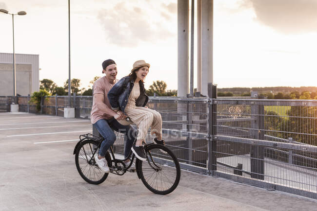Happy young couple together on a bicycle on parking deck — Stock Photo
