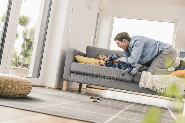 Padre che gioca con suo figlio, sdraiato sul divano — Foto stock