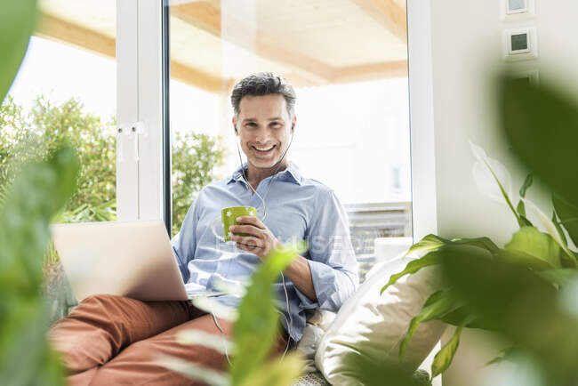 Uomo maturo seduto sul divano, usando il computer portatile, bevendo caffè — Foto stock