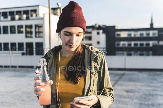 Elegante giovane donna con drink, auricolari e telefono cellulare sul ponte di parcheggio — Foto stock
