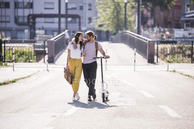 Felice giovane coppia con scooter elettrico a piedi per strada — Foto stock