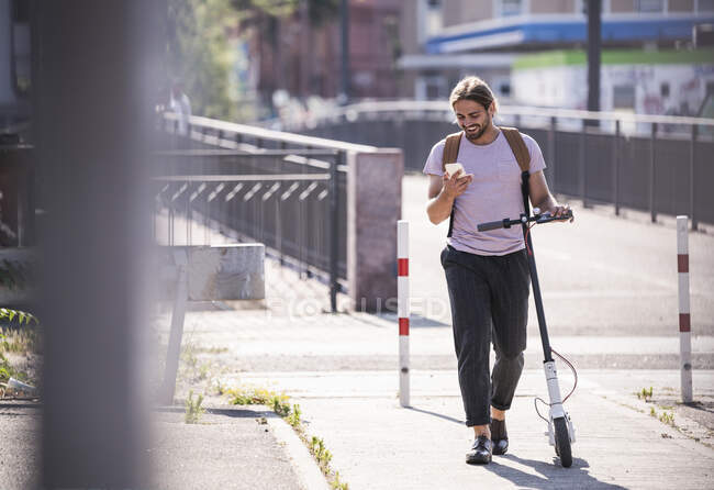 Молодой человек с электрическим скутером на улице с помощью мобильного телефона — стоковое фото