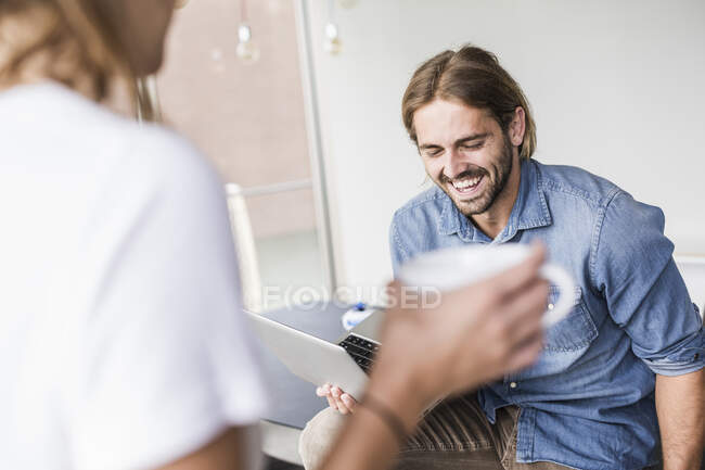 Giovane uomo d'affari ridente con laptop e donna d'affari in carica — Foto stock