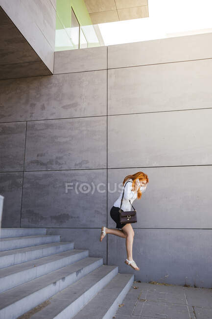 Mujer de negocios usando smartphone y saltando escaleras abajo - foto de stock