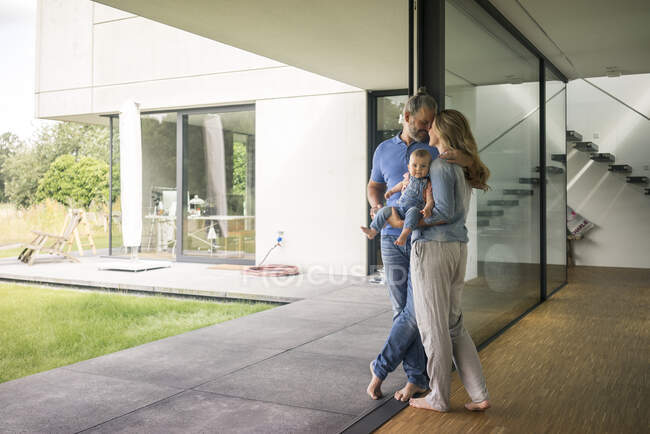 Family of three standing at the window at home — Stock Photo